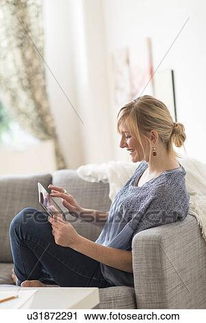 Smiling woman sitting on sofa with tablet pc View Large Photo Image Stock Image - Smiling woman sitting on sofa with tablet pc. Fotosearch