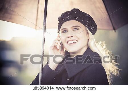 Picture - Smiling woman under umbrella using mobile phone. Fotosearch