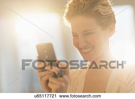Stock Image - Smiling young woman using mobile phone. Fotosearch