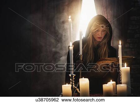 Stock Image - Sorceress reading book in dark room. Fotosearch