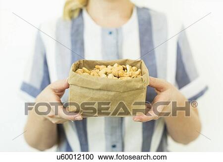 Stock Image - Studio shot of woman holding cashews in paper bag. Fotosearch
