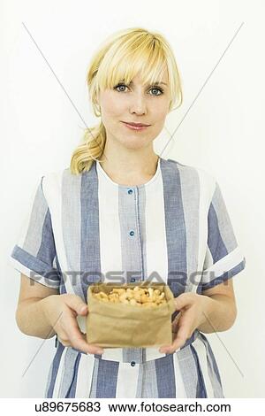 Stock Image - Studio shot of woman holding cashews in paper bag. Fotosearch
