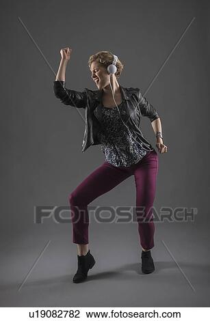 Stock Image - Studio shot of woman listening to music and dancing. Fotosearch
