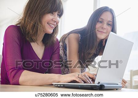 Stock Photography - Teenage girl (14-15) using laptop with her mom at home. Fotosearch