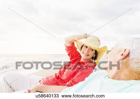View of couple sitting in lounge chairs on beach View Large Photo Image Stock Image - View of couple sitting in lounge chairs on beach . Fotosearch