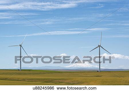 Stock Photograph - Wind turbines at green field with mountain on background. Fotosearch