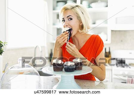Stock Photo - Woman eating muffins at kitchen. Fotosearch