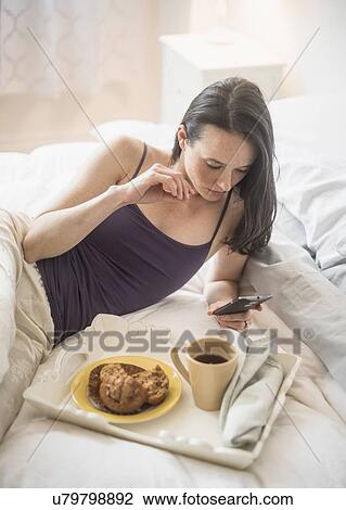 Woman having breakfast in bed, using mobile phone View Large Photo Image Stock Image - Woman having breakfast in bed, using mobile phone. Fotosearch