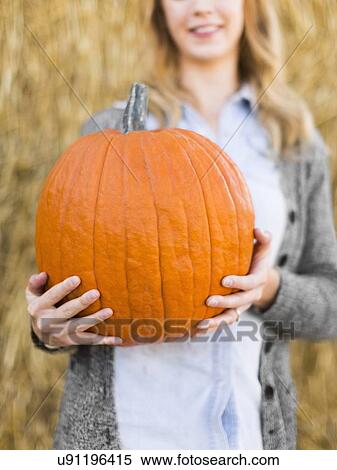 Stock Photography - Woman holding huge pumpkin in pumpkin patch. Fotosearch