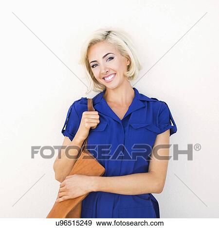 Stock Photo - Woman in blue dress and with leather bag posing to camera. Fotosearch