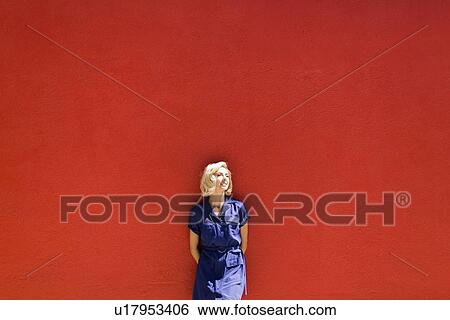 Woman in blue dress posing against red wall in sunlight View Large Photo Image Stock Photograph - Woman in blue dress posing against red wall in sunlight . Fotosearch