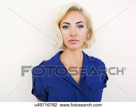 Stock Image - Woman in blue dress posing to camera against white background. Fotosearch