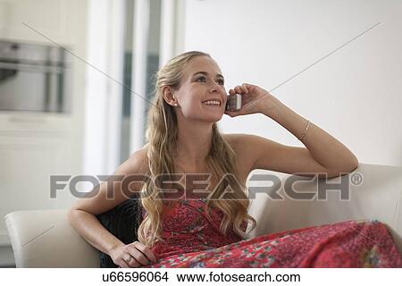 Woman in dress sitting on sofa and using phone View Large Photo Image Picture - Woman in dress sitting on sofa and using phone. Fotosearch