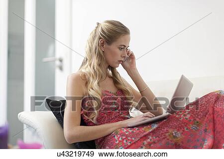 Woman in dress sitting on sofa and using phone and laptop View Large Photo Image Stock Photo - Woman in dress sitting on sofa and using phone and laptop. Fotosearch