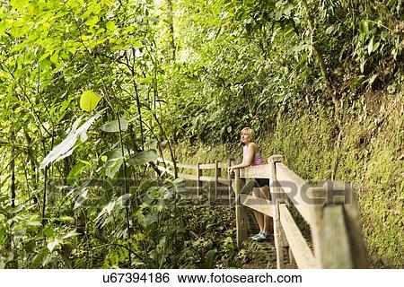 Stock Photograph - Woman in forest leaning against wooden fence. Fotosearch