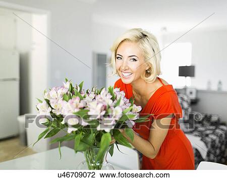 Stock Image - Woman in living room with bunch of flowers. Fotosearch