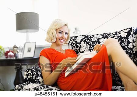 Woman in red dress lying down on sofa and holding book View Large Photo Image Stock Image - Woman in red dress lying down on sofa and holding book. Fotosearch
