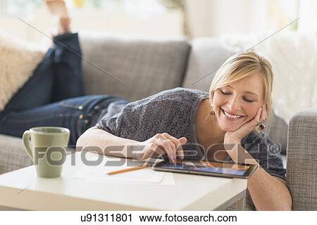Stock Image - Woman lying down on sofa with tablet pc. Fotosearch