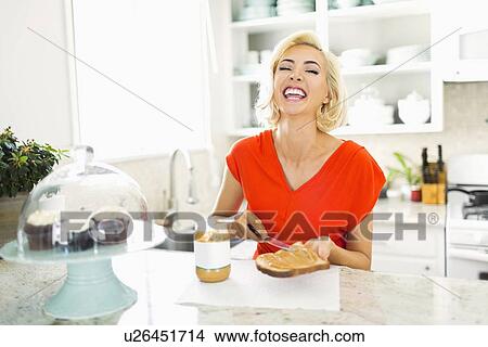 Picture - Woman making toast with peanut butter in kitchen and laughing. Fotosearch