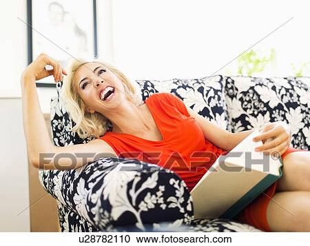 Woman on sofa holding book and laughing View Large Photo Image Stock Image - Woman on sofa holding book and laughing. Fotosearch