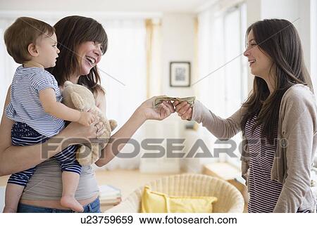 Stock Photo - Woman paying teenage nanny (14-15) for taking care of her son (12-17 months). Fotosearch