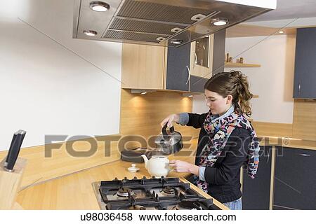 Stock Photo - Woman pouring water at teapot in kitchen. Fotosearch