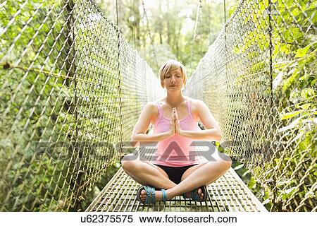 Stock Photography - Woman practicing yoga on footbridge in forest. Fotosearch