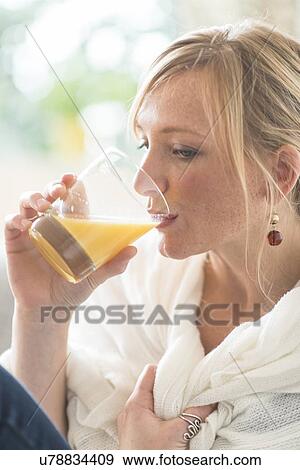 Stock Photo - Woman sitting in living room and drinking orange juice. Fotosearch