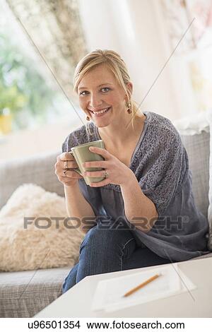 Picture - Woman sitting on sofa and drinking coffee. Fotosearch