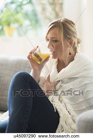 Stock Image - Woman sitting on sofa and drinking orange juice. Fotosearch