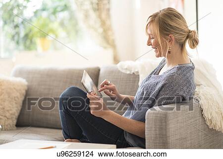 Woman sitting on sofa and using tablet pc View Large Photo Image Picture - Woman sitting on sofa and using tablet pc. Fotosearch