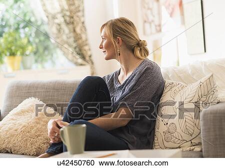 Woman sitting on sofa in living room View Large Photo Image Stock Image - Woman sitting on sofa in living room. Fotosearch