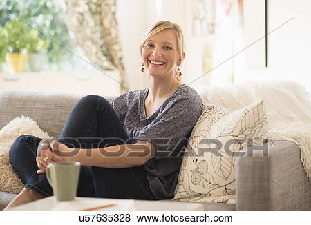 Stock Photo - Woman sitting on sofa in living room. Fotosearch