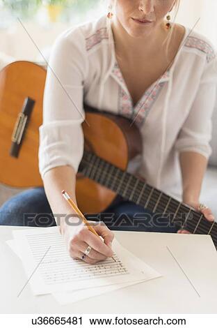 Stock Image - Woman sitting on sofa with acoustic guitar and writing. Fotosearch