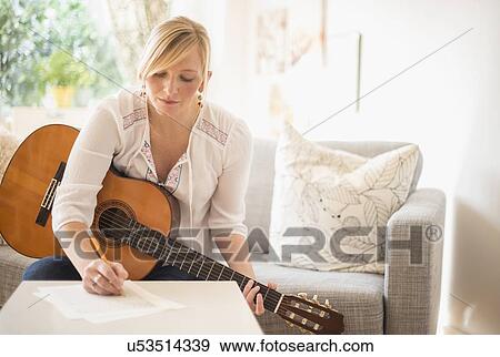 Stock Photo - Woman sitting on sofa with acoustic guitar and writing. Fotosearch
