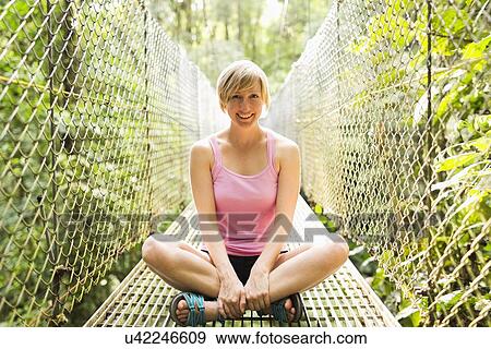 Woman sitting with legs crossed and smiling to camera on footbridge in forest View Large Photo Image Stock Photo - Woman sitting with legs crossed and smiling to camera on footbridge in forest. Fotosearch
