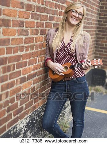 Woman standing against brick wall and playing ukulele View Large Photo Image Stock Photograph - Woman standing against brick wall and playing ukulele . Fotosearch