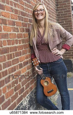 Woman standing against brick wall with ukulele View Large Photo Image Picture - Woman standing against brick wall with ukulele . Fotosearch