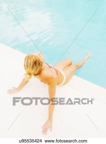 Woman sunbathing next to swimming pool View Large Photo Image Picture - Woman sunbathing next to swimming pool. Fotosearch