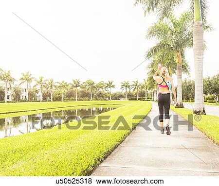Stock Photo - Woman walking along promenade drinking water. Fotosearch