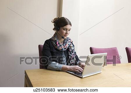 Stock Image - Woman wearing headset working on laptop. Fotosearch