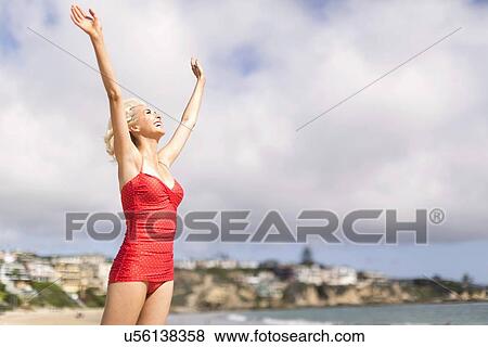 Woman wearing red one piece swimsuit standing on beach with arms raised View Large Photo Image Stock Photo - Woman wearing red one piece swimsuit standing on beach with arms raised. Fotosearch