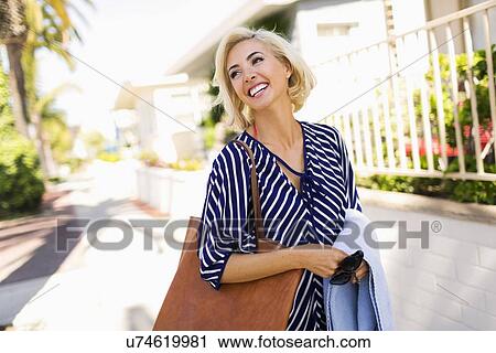 Stock Image - Woman wearing striped blouse walking street and smiling. Fotosearch