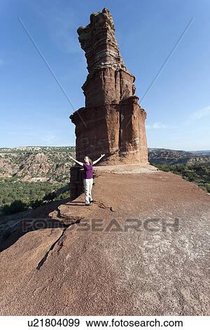 Stock Photo - Woman with arms outstretched standing by rock formation. Fotosearch