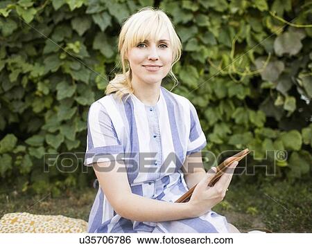 Woman with digital tablet sitting in garden View Large Photo Image Stock Photograph - Woman with digital tablet sitting in garden. Fotosearch
