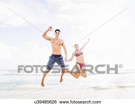 Young couple jumping on beach, holding hands View Large Photo Image Stock Photograph - Young couple jumping on beach, holding hands. Fotosearch