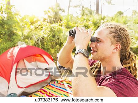 Stock Photograph - Young man watching birds through binoculars. Fotosearch