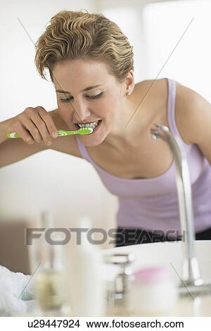 Picture - Young woman brushing teeth in bathroom. Fotosearch