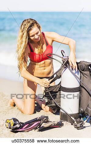 Young woman kneeling on sandy beach putting together scuba diving equipment View Large Photo Image Stock Photo - Young woman kneeling on sandy beach putting together scuba diving equipment. Fotosearch