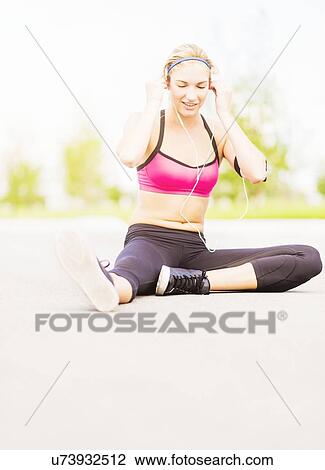 Young woman listening to music while stretching View Large Photo Image Stock Image - Young woman listening to music while stretching. Fotosearch